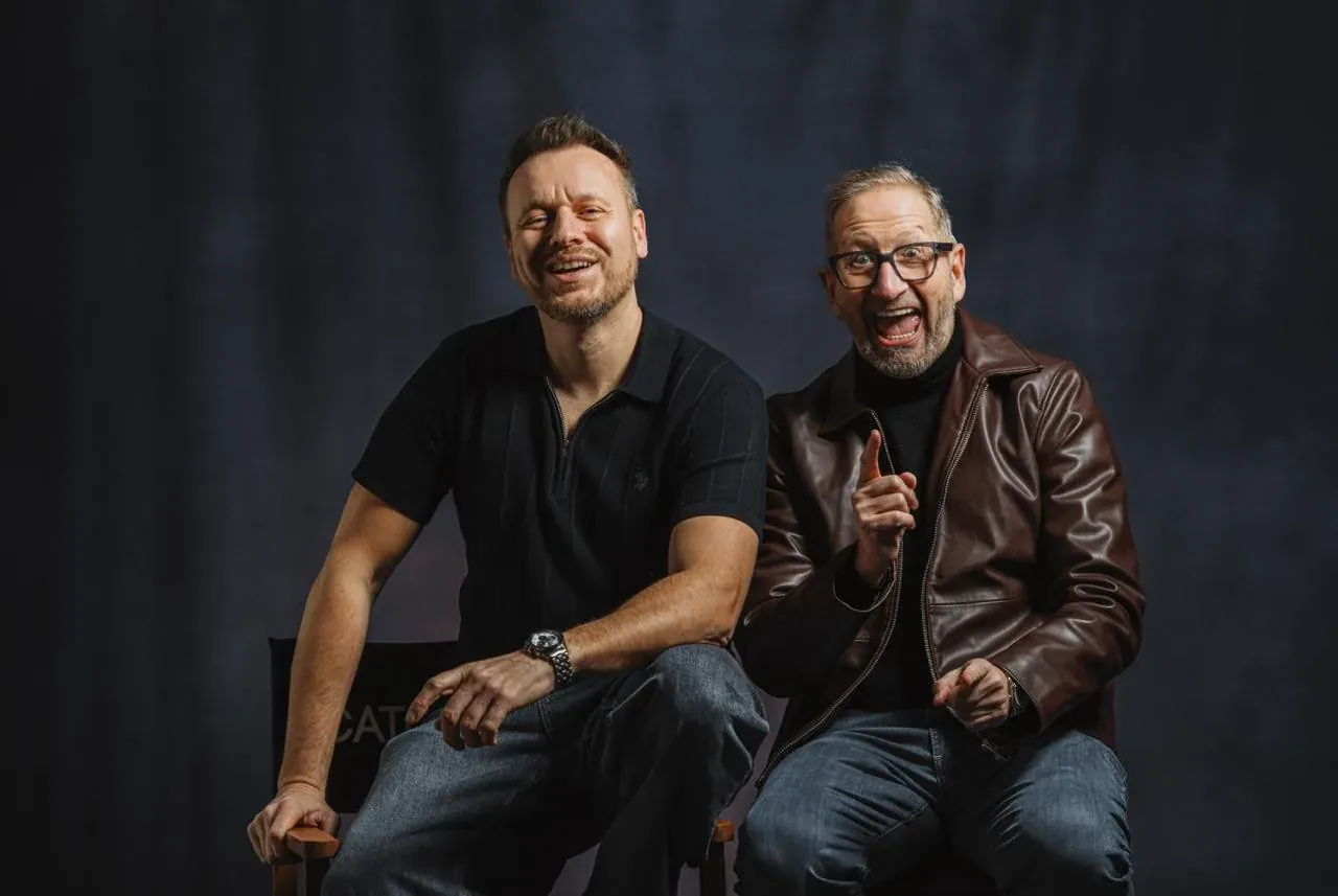 Chris and Henry seated together against a dark studio backdrop