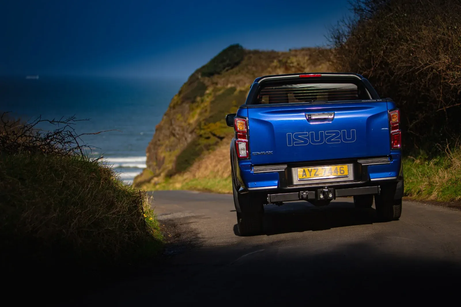 Rear view of a blue pickup on a coastal road