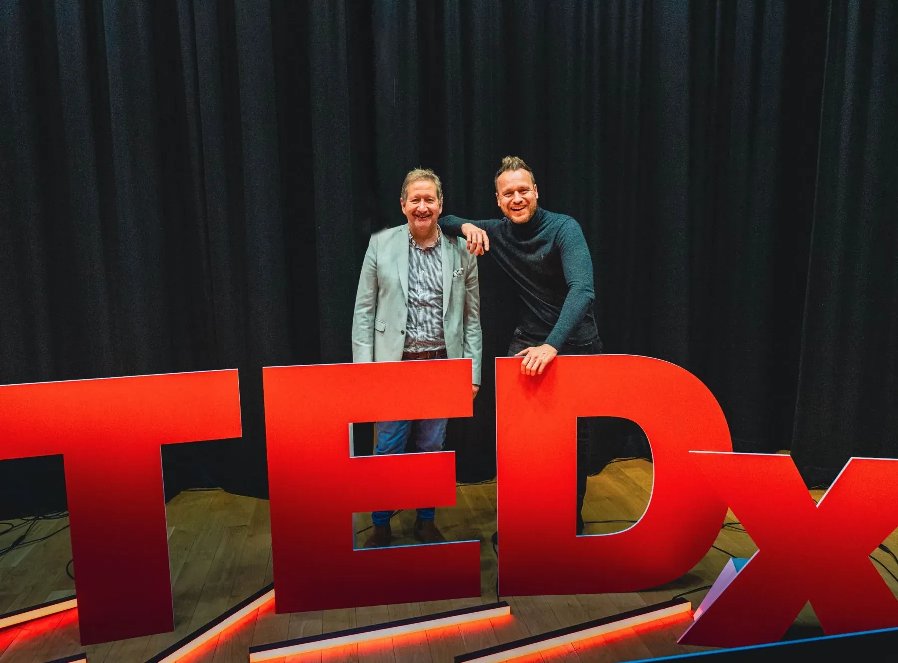 Two people standing beside large TEDx letters at an event